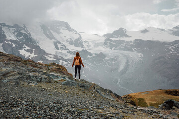 Fototapeta premium Girl, woman with backpack in the leather jacket on the mountain background. Top of the Gornergrat near Matterhorn, Zermatt, Switzerland. Swiss Alps hiking. Adventure in Europe. Tourist.