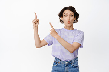 Wow impressive. Excited young woman showing banner, advertisement at upper left corner, pointing at copy space with amazed face, white background