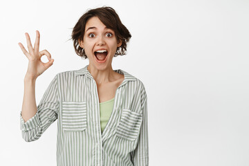 Surprised brunette girl shows okay, ok sign, look amazed, praise smth good, positive feedback,...