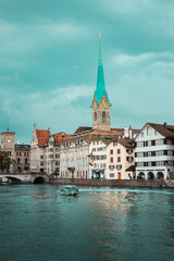 Fototapeta premium Old town in Zurich city, Switzerland. Panorama of river, bridge, church with a spire and embankment with historic buildings. Pleasure boat. Swiss vacation.