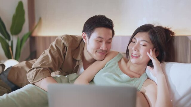 love marry couple happiness cheerful watching streaming movie together on the bed,home isolation ideas concept asian husband and wife lay down clam and joyful on the bed