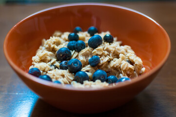 Tasty oatmeal porridge with blueberries and maple syrup in orange bowl.  Healthy breakfast meal. Close up.