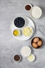 Cake ingredients: flour, butter, baking powder, chocolate, blueberries, eggs, cocoa, sugar, whisk on a light background. Ingredients for a chocolate blueberry pie recipe top view. 