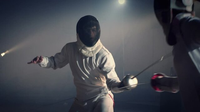 Footage of two fencing athletes duel . Two Professional Fencers Show Masterful Swordsmanship in their Foil Fight. Fencing training . Shot on ARRI ALEXA camera . 