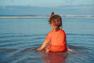 Toddler girl playing in the water on beautiful sandy tropical beach in summer vacation at sunset