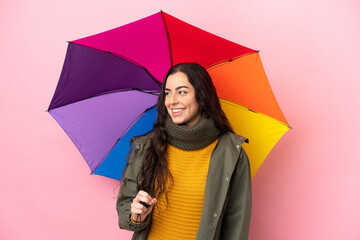 Young woman holding an umbrella isolated on pink background looking side