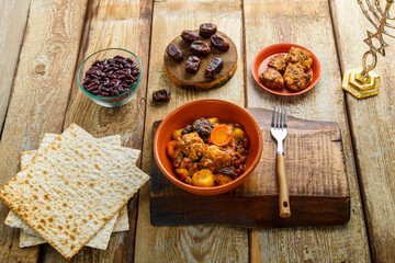 Jewish dish shuttle with meat in a dish on a wooden table near matzo and ingredients.