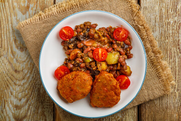 Cod cutlets with stewed potatoes and vegetables on a plate on a napkin.