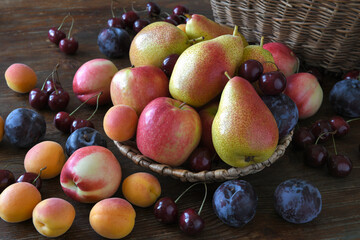 Summer harvest of fruits, pears, apples, plums, cherries in a wicker basket on a dark wooden table. Still life in a rustic style. 