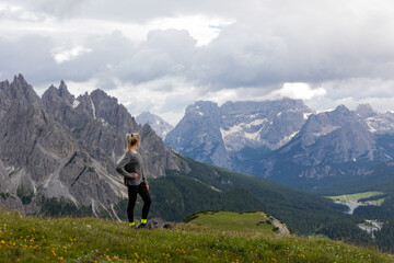 Fit blond hiking girl standing on top of the mountain looking into the valley