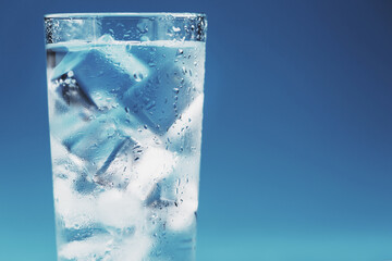 Glass with water and ice cubes on a blue background