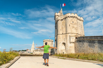 A young man on vacation next to Saint Nicolas Tower of La Rochelle in the summer. Coastal town in...