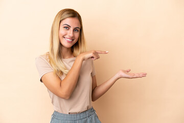 Blonde Uruguayan girl isolated on beige background holding copyspace imaginary on the palm to...