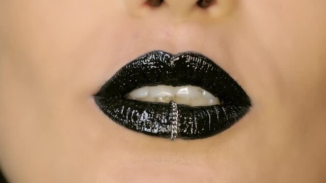 Closeup of a beautiful woman lips with beautiful black makeup and piercing sending air kiss . Close up of girl's mouth having flirty emotions and sending air kiss .