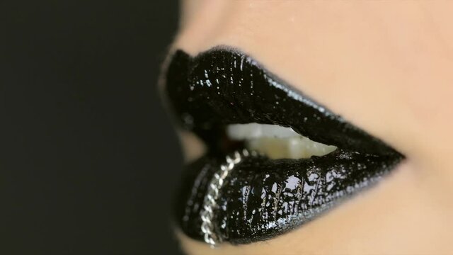Closeup of a beautiful woman lips with beautiful black makeup and piercing sending air kiss . Close up of girl's mouth having flirty emotions and sending air kiss .
