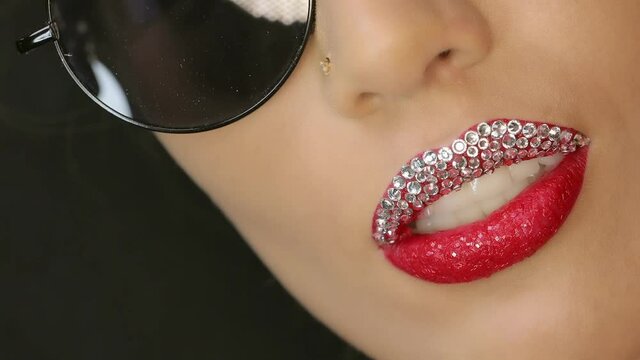 Closeup of a beautiful woman lips with beautiful diamond, red make up and sunglasses sending air kiss . Close up of girl's mouth having flirty emotions and sending air kiss .