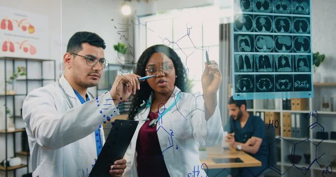 View through glass board where confident high-skilled mixed race two male and female chemists which working with structural formulas drawn on this board
