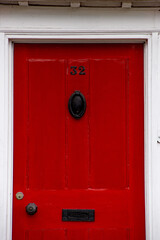 The house number 32 on a red wooden painted front door frame in Hertfordshire, with a brass door knocker, and letter box with handle.