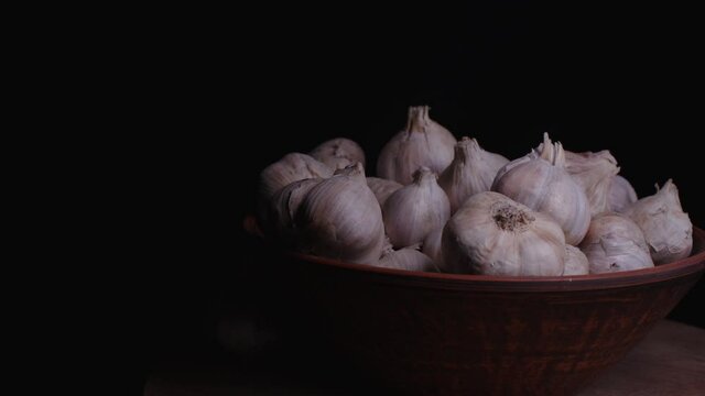 Pile of whole bulbs of garlic in ceramic bowl on table. Harvest of unpeeled vegetables on black background