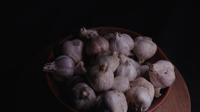 Pile of whole bulbs of garlic in ceramic bowl on table. Harvest of unpeeled vegetables on black background