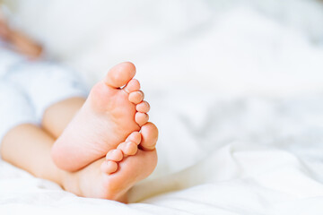 Close up barefoot baby feet lying on white bed linen. Fabric softener, cleanliness. Space for message - obrazy, fototapety, plakaty