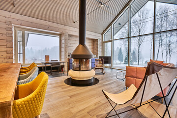 Country house living room interior with panoramic windows with sofa and stove, natural wood parquet and walls