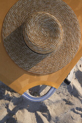  Straw hat and orange sunbed on sand beach, no people. Idyllic and tranquil summer vacation concept.