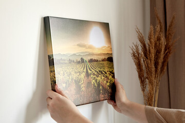 Canvas print with gallery wrap and dry grass interior decor. Woman hangs landscape photography on...