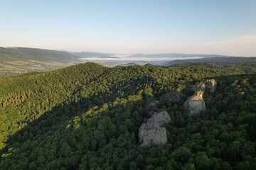 Summer panorama of Ukrainian mountain range. Beautiful summer scenery. Morning fog spreads on the mountain valley. Panoramic summer scene of Carpathian village. Amazing morning landscape of mountain. 