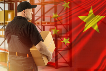 Worker with box and flag of China. Concept is warehouse company in China. Shelving in background...