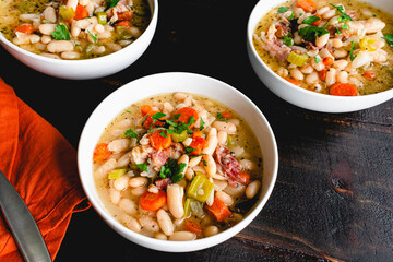 Bowls of White Bean and Ham Soup with Bread: Three bowls of cannellini bean soup with smoked pork...