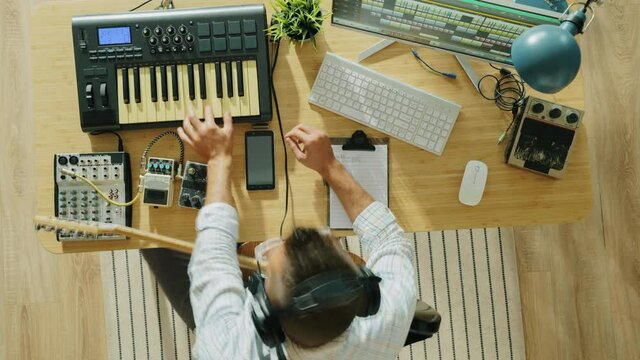 Top view time lapse of young man creating music playing keyboard and electric guitar at home. Guy is using modern equipment and taking notes.