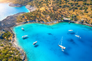 Aerial view of beautiful yachts and boats on the sea at sunset in summer. Akvaryum koyu in Turkey. Top view of luxury yachts, sailboats, clear blue water, rock, lagoon, mountain, green trees. Travel