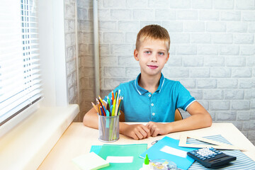 Boy is sitting at school desk. Stationery is laid out on table near the child.