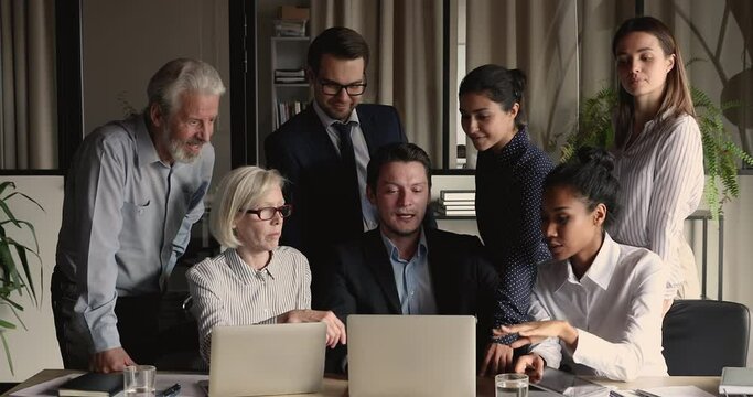 Seven diverse employee make team building task cooperate think over project gathered together in modern office workplace use laptop discuss new corporate app consider current business at group meeting