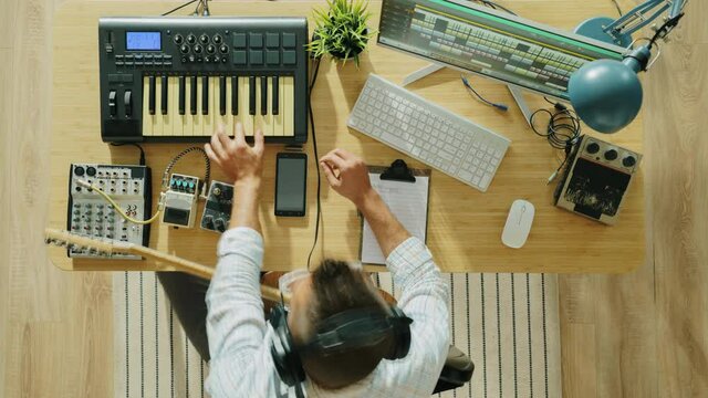 Zoom-in time lapse of creative guy recording music playing instruments guitar and keyboard taking notes and mixing audio with modern equipment
