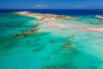 Aerial view of shallow sandy lagoons and a beach surrounded by deeper dark blue sea (Elafonissi Beach)