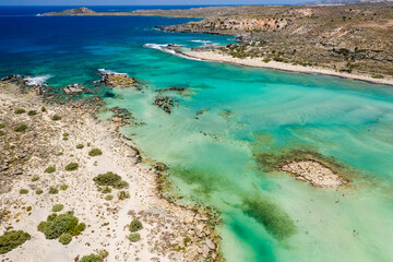Aerial view of shallow sandy lagoons and a beach surrounded by deeper dark blue sea (Elafonissi Beach)
