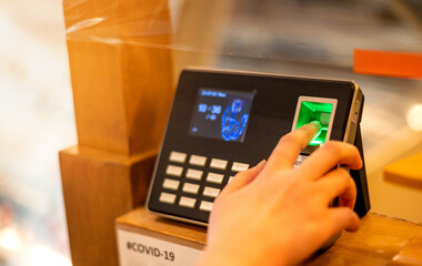 Closeup woman employee using biometric fingerprint machine for attendance system with a numeric keypad at work