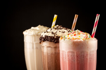 Three glasses of milkshake with assorted flavors. Chocolate, vanilla and strawberry milkshake.