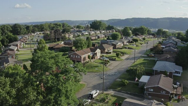 An aerial forward view above a typical Pennsylvania residential neighborhood. Factories along the Ohio River in the distance. Pittsburgh suburbs.  	