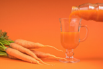 The process of filling a glass glass with a carrot smoothie on an orange background.