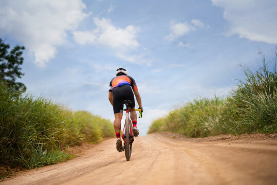 Asian Man Cycling On Gravel Road.