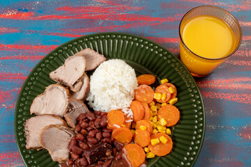 typical Brazilian food dish with rice, red beans, pork and carrot salad and braised corn