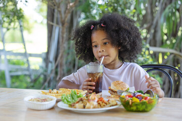 Childhood and healthy concept - Little African American curly hair girl with american food various and soft drink on table.