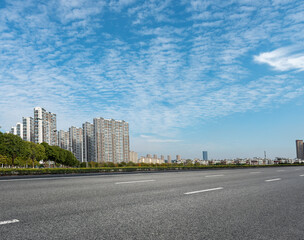 Fototapeta na wymiar The black asphalt road next to the city's high-rise buildings