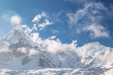 Obraz premium Beautiful snowy mountain peak in clouds and sunrays at sunset or sunrise. Sagarmatha Zone, Nepal
