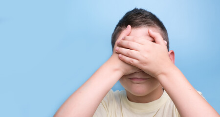 Boy covering face with hands being thoughtful, doubter and unsuspecting, showing true emotion.