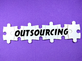 Text OUTSOURCING on jigsaw puzzle on a purple background.