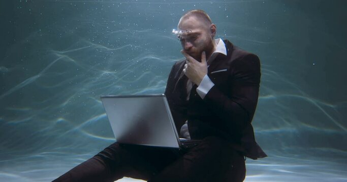 Creative occupation concept. Young happy businessman in suit thinking, using laptop to work under water slow motion.